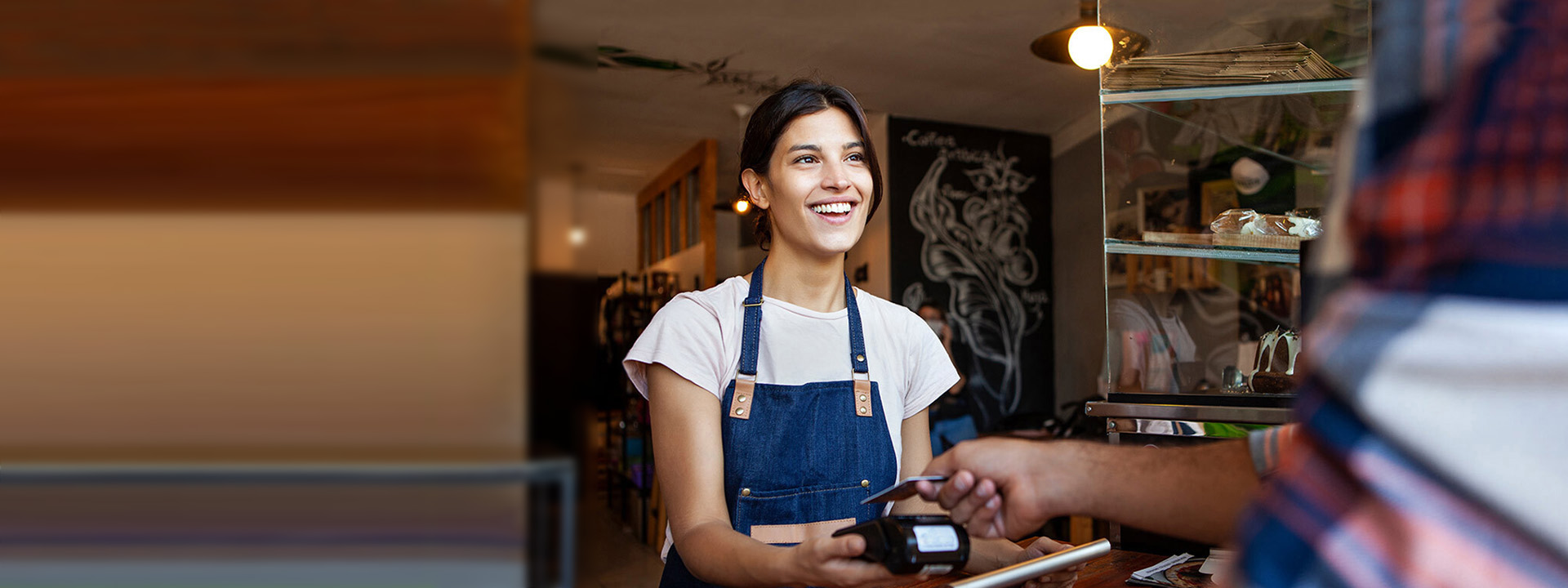 Mujer sonriente recibiendo un pago de una clienta en una cafetería